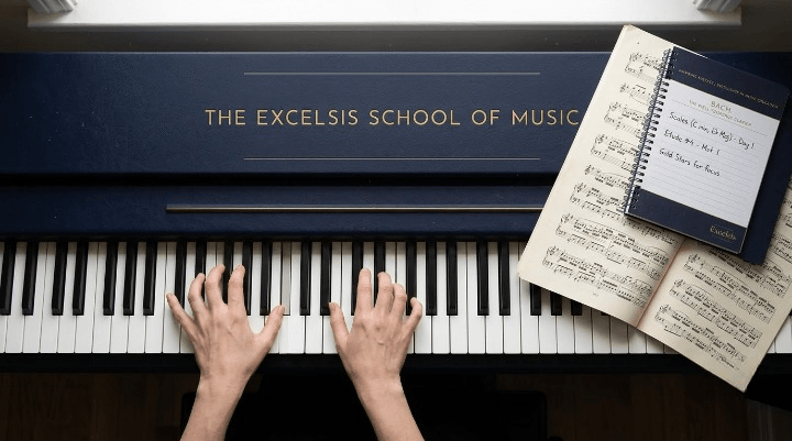 Hands playing piano keys next to an open practice diary and sheet music