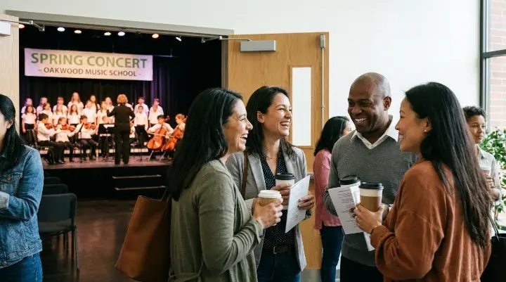 Parents chatting at a music school event while children perform in the background
